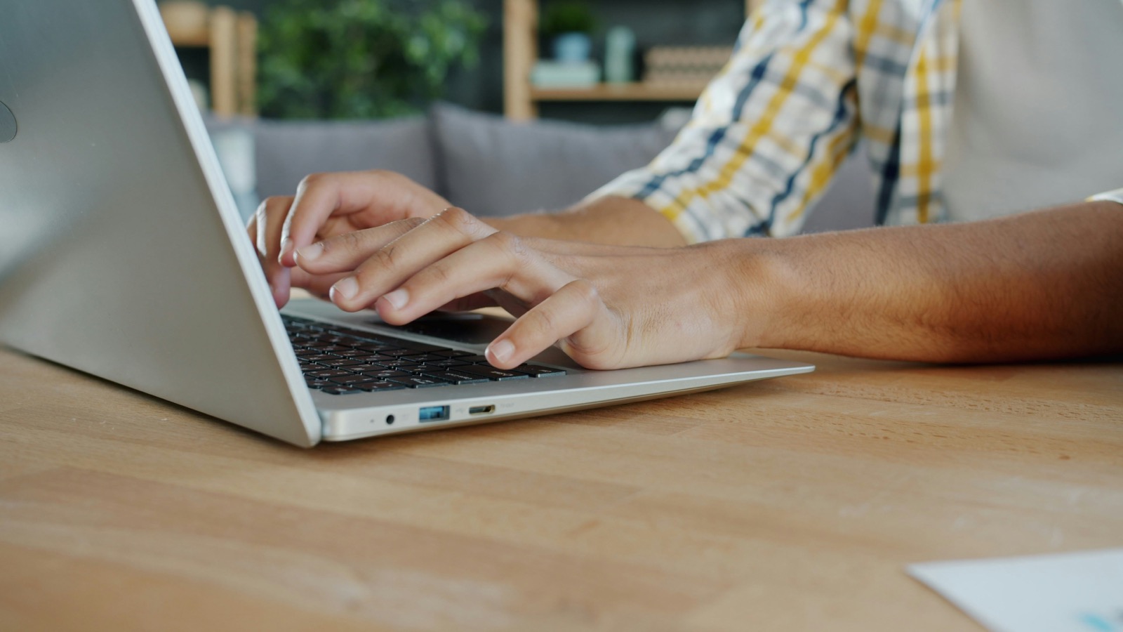Manos escribiendo en el teclado de un notebook sobre un escritorio de madera