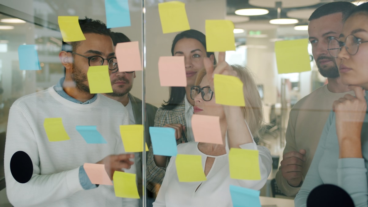 Equipo ordenando ideas con notas adhesivas sobre un panel de vidrio